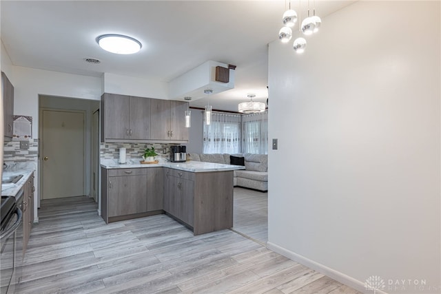 kitchen featuring light hardwood / wood-style floors, kitchen peninsula, tasteful backsplash, a notable chandelier, and black range