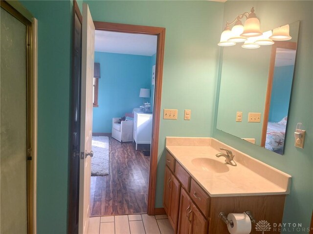 bathroom with wood finished floors, an inviting chandelier, connected bathroom, vanity, and baseboards
