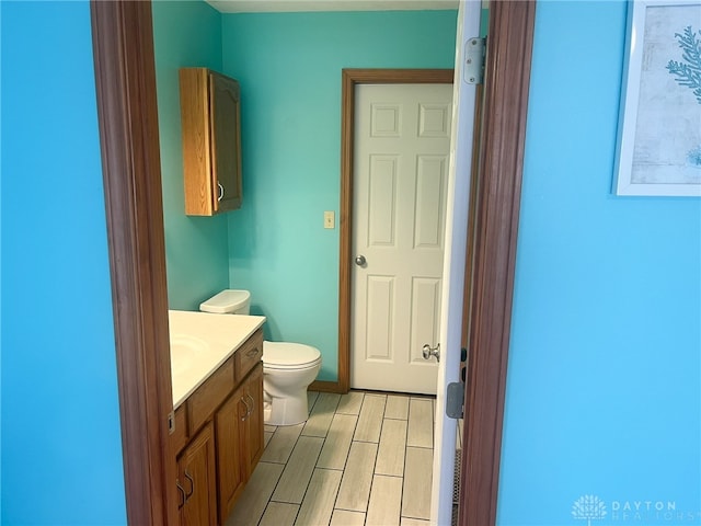 half bath featuring wood finish floors, toilet, and vanity
