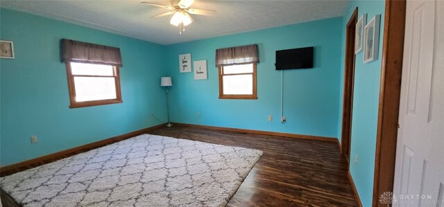 unfurnished room with baseboards, a healthy amount of sunlight, dark wood-style flooring, and ceiling fan