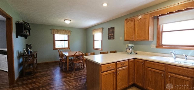 kitchen featuring dark wood finished floors, light countertops, brown cabinets, a sink, and a peninsula