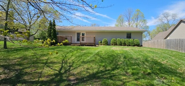 back of property with a deck, a yard, and fence