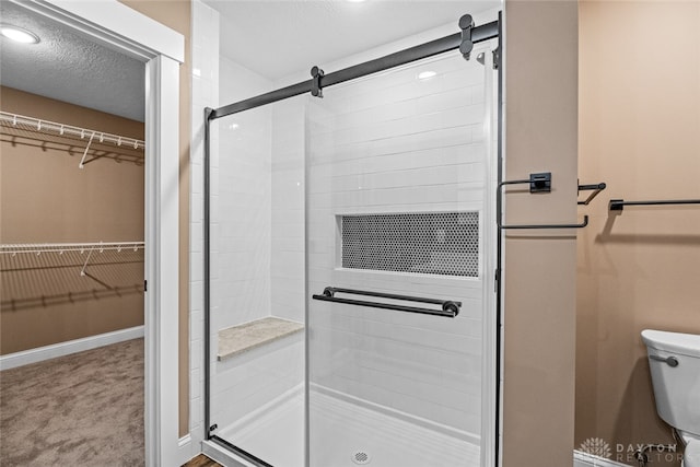 bathroom featuring toilet, a shower with door, and a textured ceiling