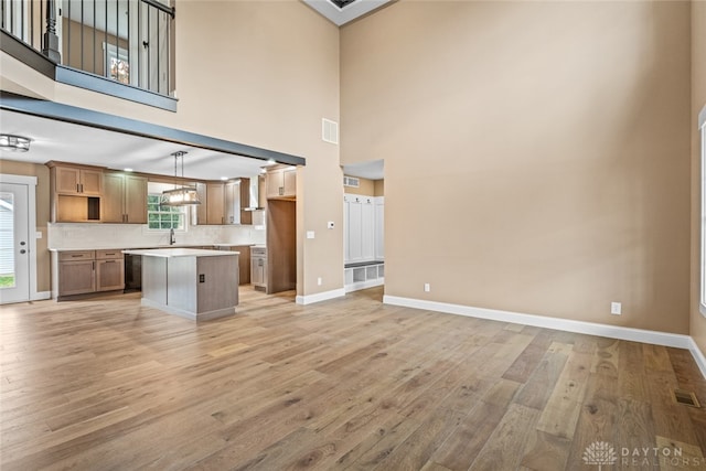 kitchen with pendant lighting, a kitchen island, light wood-type flooring, and a towering ceiling