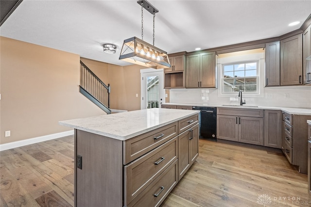 kitchen featuring light wood-type flooring, sink, decorative light fixtures, black dishwasher, and a kitchen island