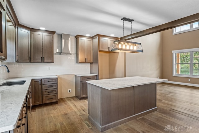 kitchen with pendant lighting, sink, hardwood / wood-style flooring, wall chimney exhaust hood, and a kitchen island