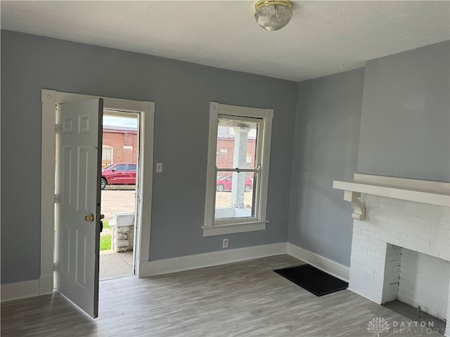 unfurnished living room with a textured ceiling, hardwood / wood-style flooring, a brick fireplace, and plenty of natural light