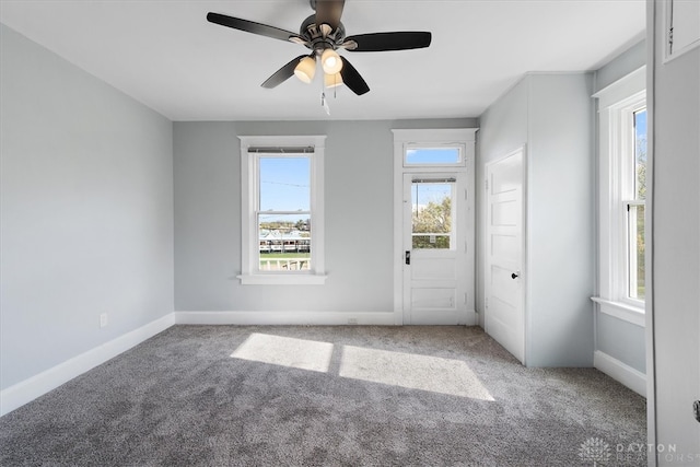 empty room with a wealth of natural light, ceiling fan, and carpet flooring