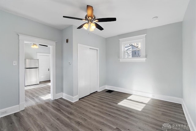 unfurnished bedroom featuring a closet, wood-type flooring, stainless steel refrigerator, and ceiling fan