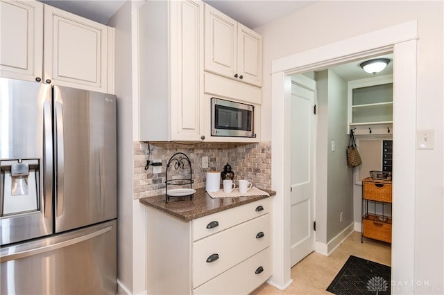 kitchen featuring dark stone counters, white cabinets, light tile patterned floors, appliances with stainless steel finishes, and tasteful backsplash