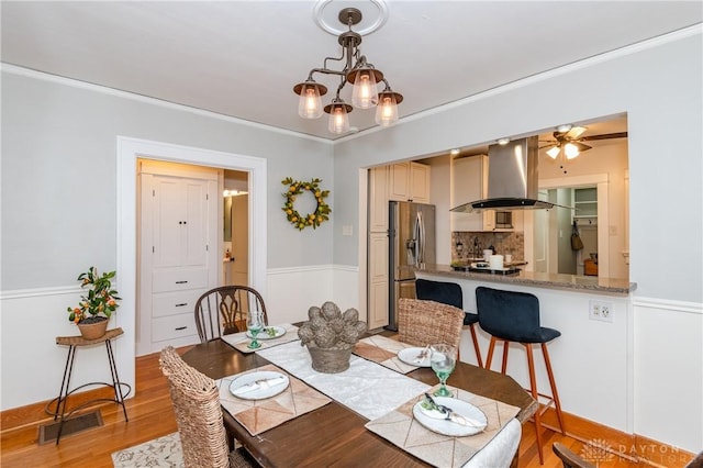 dining space featuring ceiling fan with notable chandelier, light wood-type flooring, and crown molding