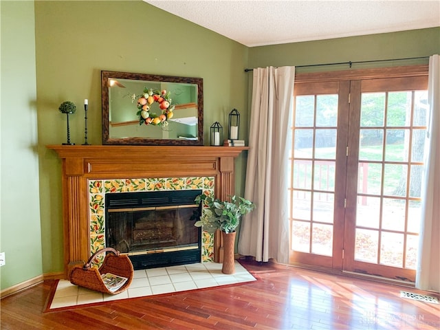 living area featuring a tiled fireplace, plenty of natural light, lofted ceiling, and light wood-type flooring