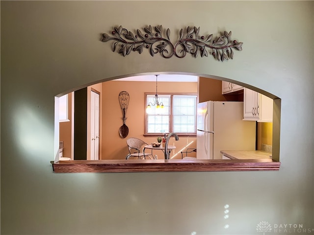 kitchen featuring pendant lighting, white refrigerator, sink, white cabinetry, and a chandelier