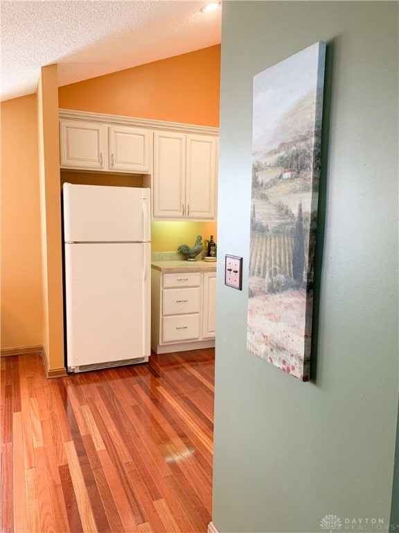 kitchen with white refrigerator, vaulted ceiling, light wood-type flooring, a textured ceiling, and white cabinetry