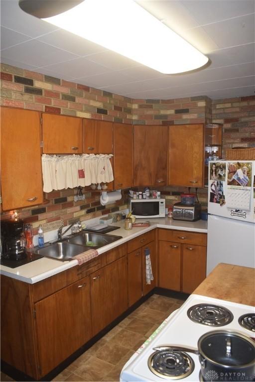 kitchen featuring sink, white appliances, and brick wall