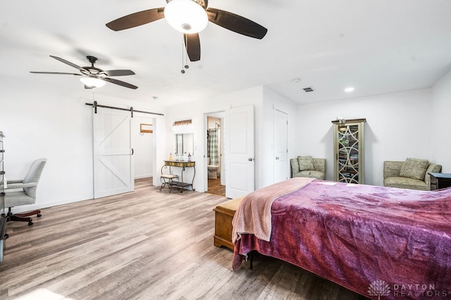 bedroom featuring light wood-type flooring, a barn door, ensuite bath, and ceiling fan