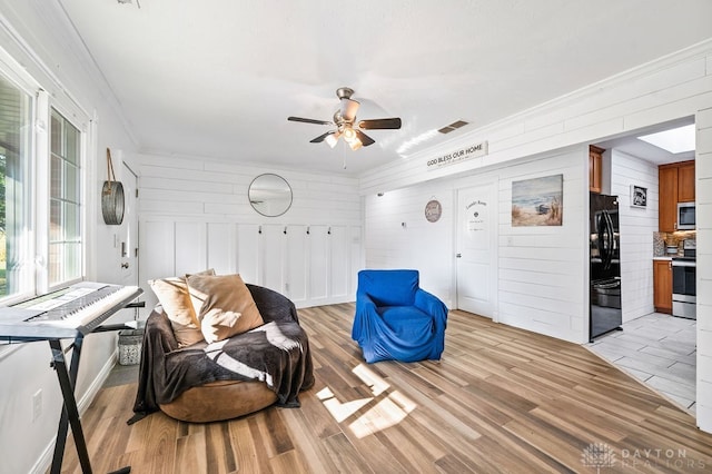 sitting room with light wood-type flooring, ceiling fan, and wood walls