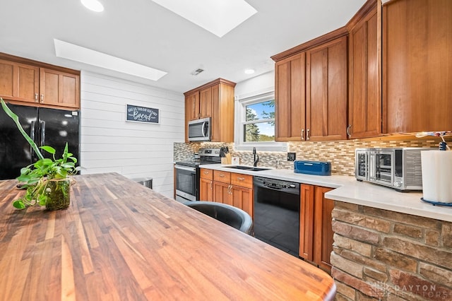 kitchen with black appliances, decorative backsplash, butcher block counters, and a skylight