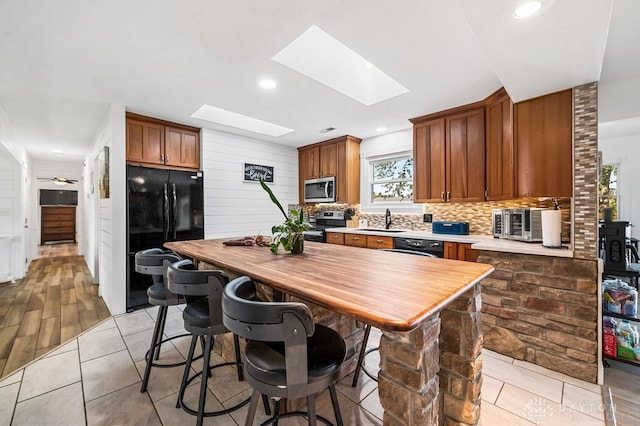 kitchen featuring sink, light wood-type flooring, a skylight, and black appliances