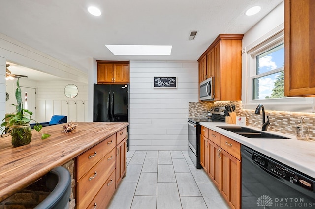 kitchen featuring a skylight, sink, wooden counters, wooden walls, and black appliances