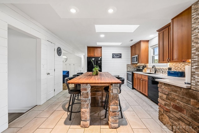 kitchen featuring black appliances, a kitchen breakfast bar, sink, a skylight, and tasteful backsplash