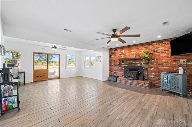 unfurnished living room with ceiling fan, light wood-type flooring, and a wood stove