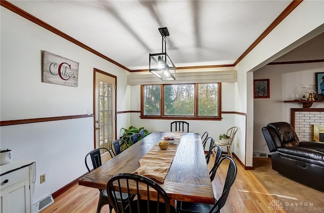 dining space with a fireplace, light hardwood / wood-style floors, and crown molding