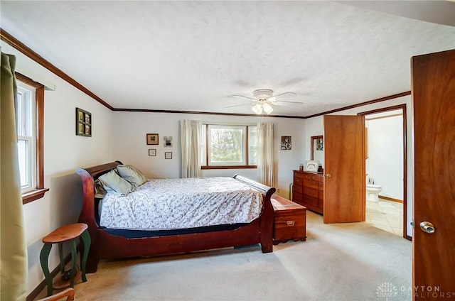 bedroom featuring ceiling fan, light colored carpet, ornamental molding, and ensuite bath