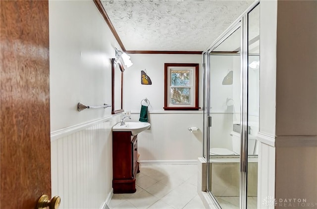 bathroom with vanity, a shower with shower door, a textured ceiling, and ornamental molding