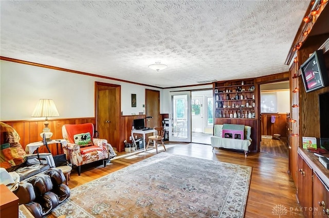 living room with french doors, a textured ceiling, wooden walls, crown molding, and wood-type flooring