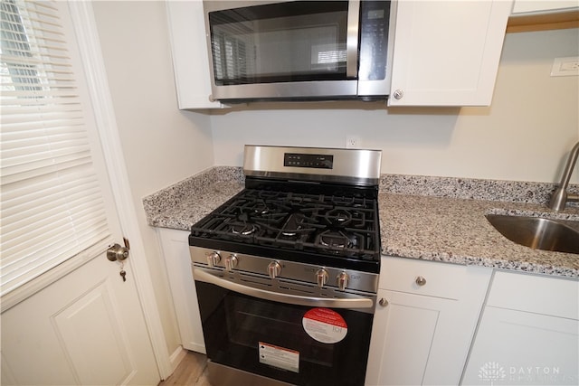 kitchen featuring white cabinetry, sink, light stone counters, and appliances with stainless steel finishes