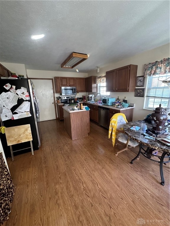 kitchen with a center island, sink, hardwood / wood-style flooring, a textured ceiling, and appliances with stainless steel finishes