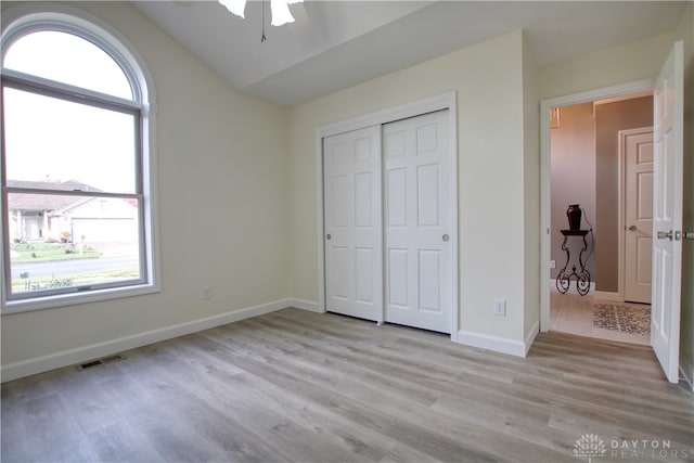 unfurnished bedroom featuring multiple windows, a closet, light hardwood / wood-style floors, and lofted ceiling