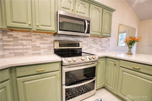 kitchen featuring decorative backsplash, stainless steel appliances, light tile patterned floors, green cabinetry, and lofted ceiling