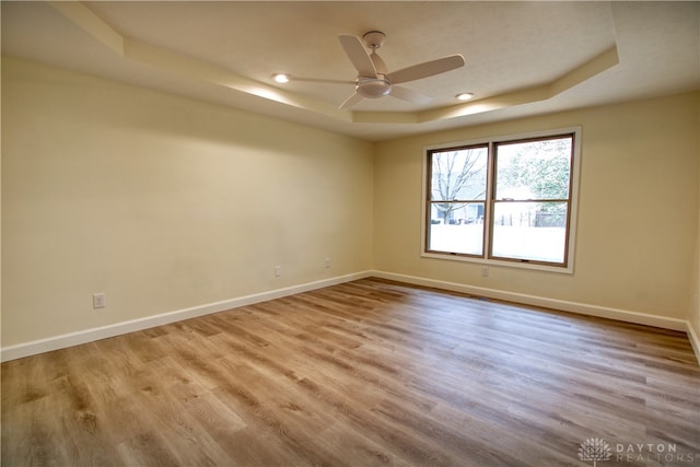 empty room with ceiling fan, a raised ceiling, and light wood-type flooring