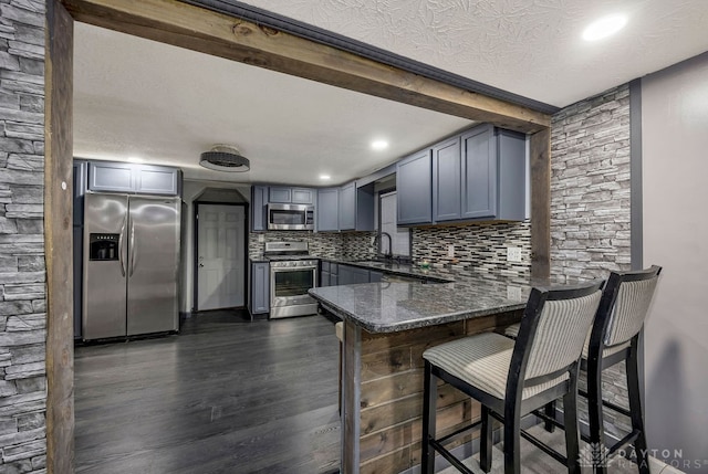 kitchen with dark wood-type flooring, backsplash, kitchen peninsula, a textured ceiling, and appliances with stainless steel finishes