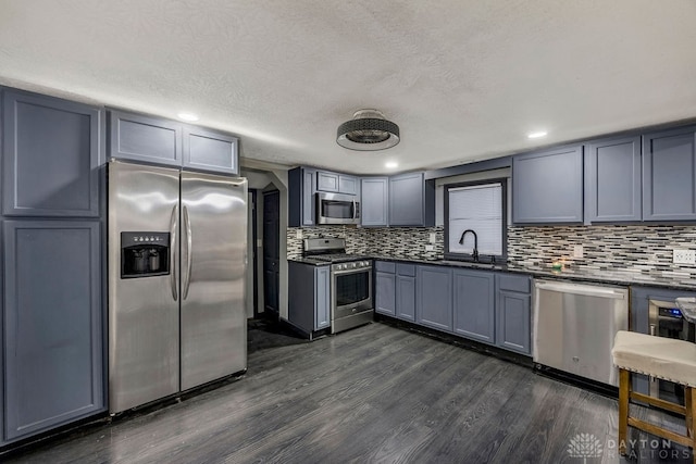 kitchen featuring sink, decorative backsplash, a textured ceiling, appliances with stainless steel finishes, and dark hardwood / wood-style flooring