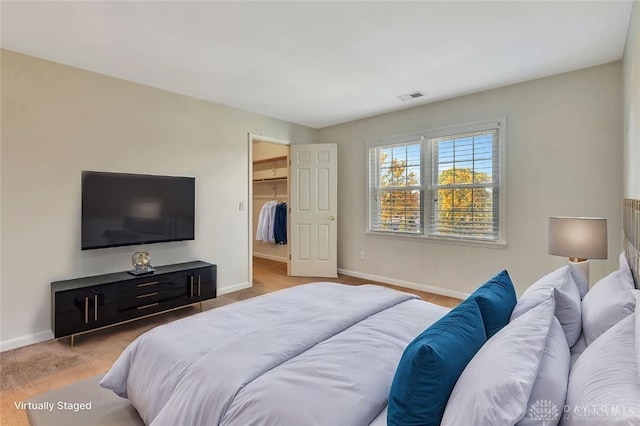 bedroom with a walk in closet, light colored carpet, and a closet