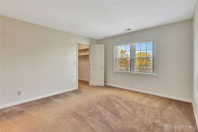 unfurnished bedroom with a spacious closet, a closet, and light colored carpet