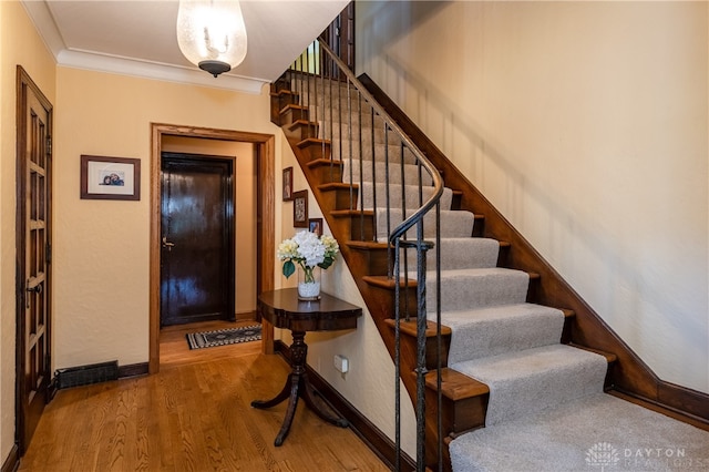 stairway with wood-type flooring and ornamental molding