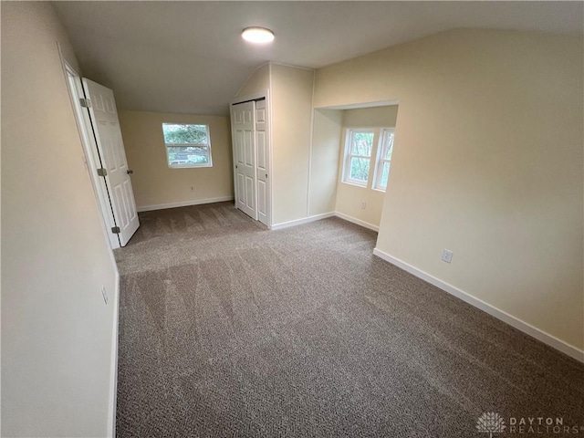 unfurnished bedroom featuring carpet floors, a closet, vaulted ceiling, and multiple windows