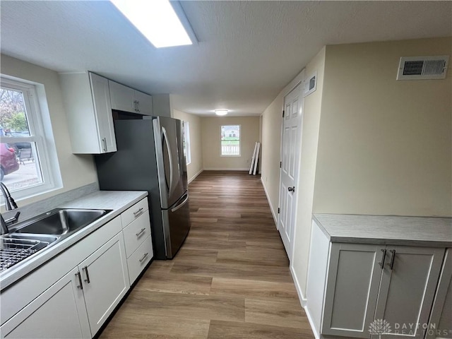 kitchen with white cabinets, light wood-type flooring, a wealth of natural light, and sink