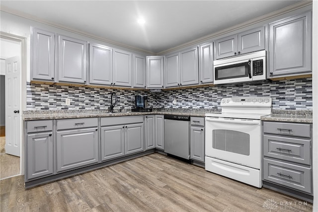 kitchen with backsplash, gray cabinetry, light wood-type flooring, and appliances with stainless steel finishes