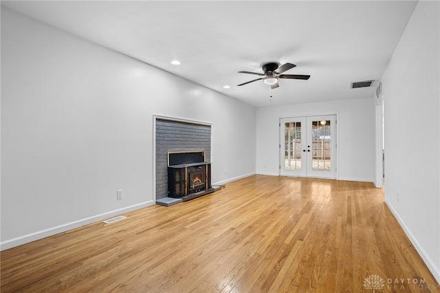 unfurnished living room featuring a fireplace, ceiling fan, french doors, and light hardwood / wood-style floors