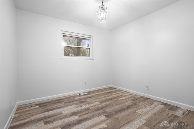 unfurnished room with hardwood / wood-style floors and an inviting chandelier