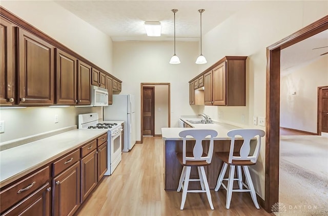 kitchen with white appliances, decorative light fixtures, sink, a kitchen breakfast bar, and light hardwood / wood-style flooring