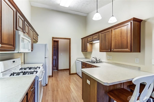 kitchen with white appliances, light hardwood / wood-style floors, sink, hanging light fixtures, and a breakfast bar