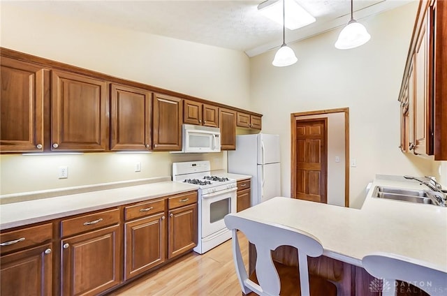 kitchen with a kitchen bar, light hardwood / wood-style floors, decorative light fixtures, white appliances, and sink