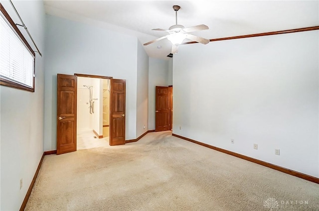 interior space with a high ceiling, ensuite bath, ornamental molding, ceiling fan, and light colored carpet