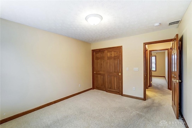 unfurnished bedroom with light carpet, a closet, and a textured ceiling